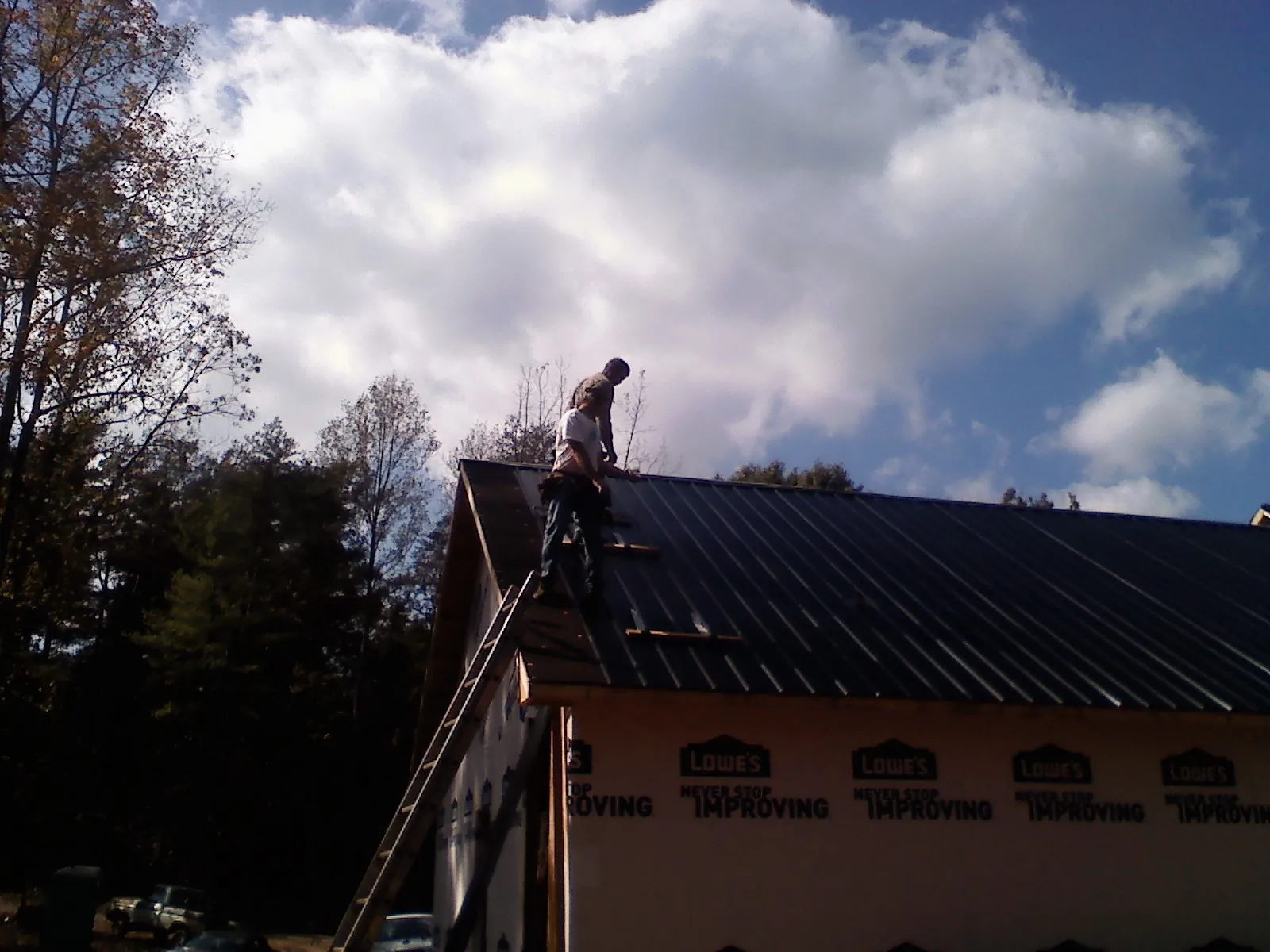 Roofer fastening dark metal panels high against a cloudy sky, from a Roof Inspection job in Fairview
