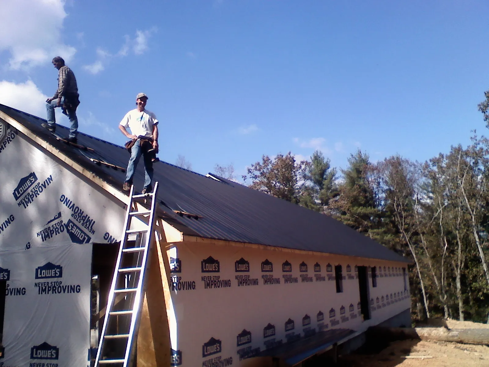 Two roofers standing on a long dark metal roof over a wrapped building in Fairview
